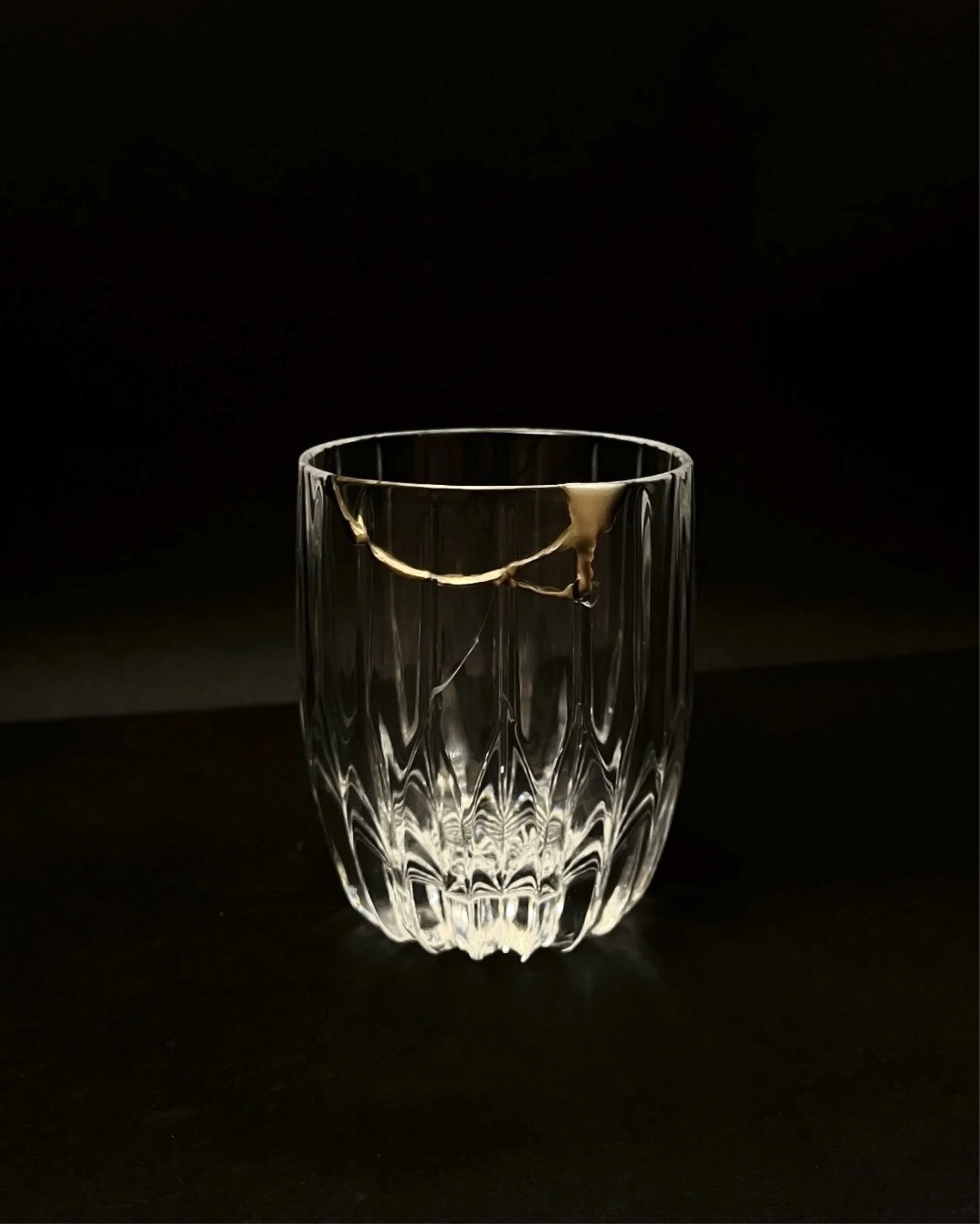 A cut-glass tumbler with a gold repair line, lit against a dark ground.