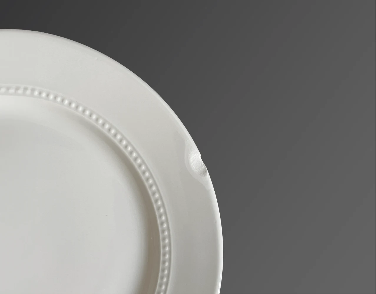 The beaded rim of a white plate with a small chip missing.